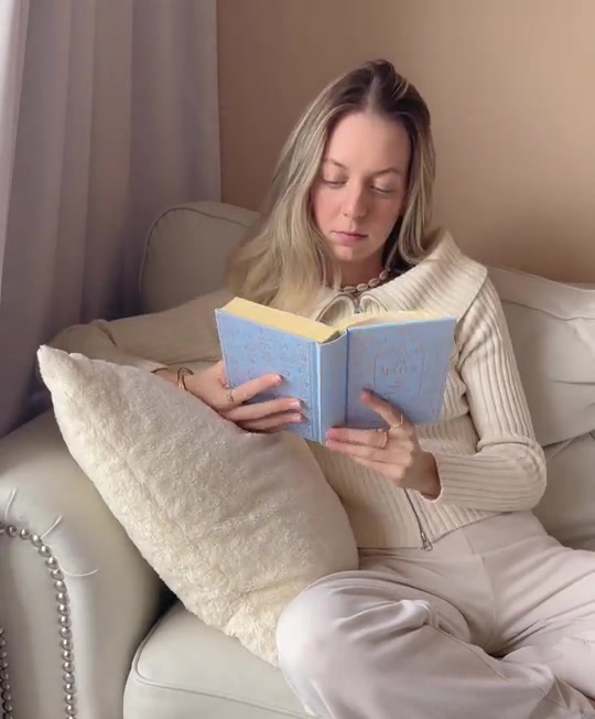 Emma reading a book on a cream sofa in a bright living room